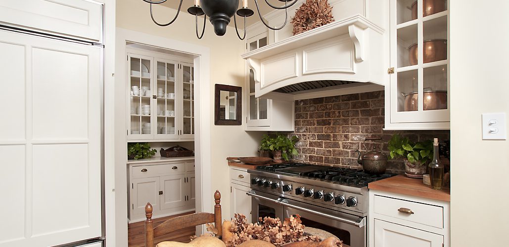 White kitchen with a brick backsplash, professional range and glass-front cabinets