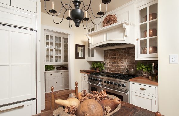 White kitchen with a brick backsplash, professional range and glass-front cabinets