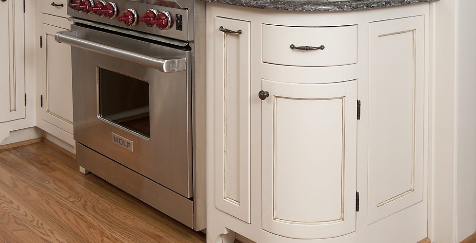 Stainless range beside white cabinetry with a rounded end cabinet