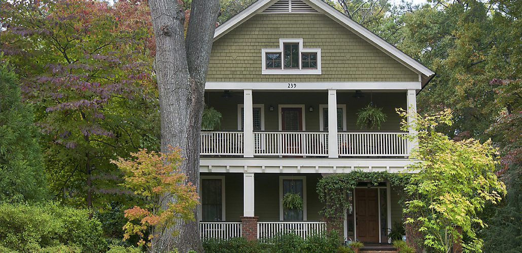 Sage-green two-story custom home with a double front porch and shade tree