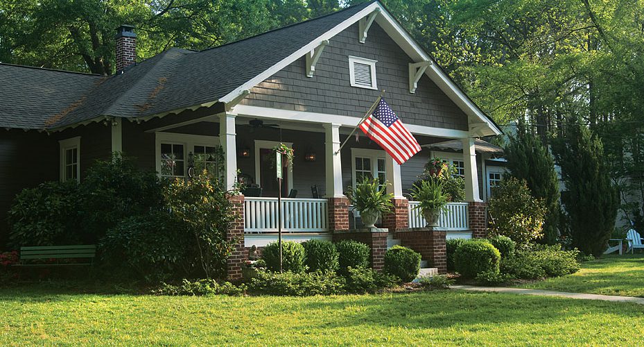 Craftsman bungalow with a covered front porch, American flag and green lawn