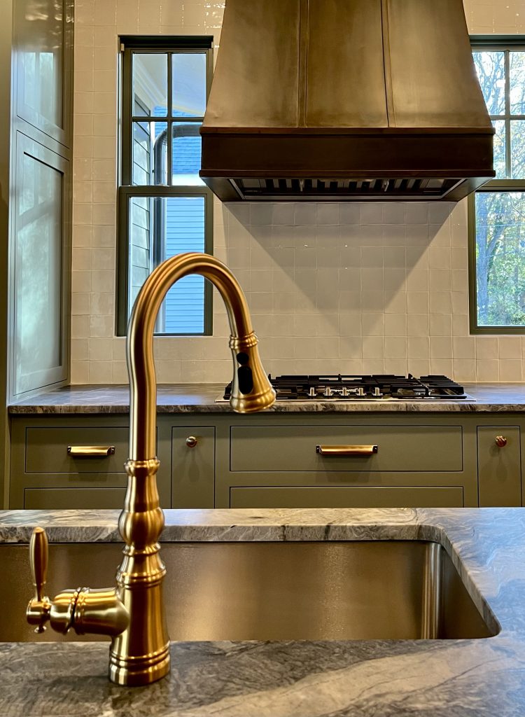 Kitchen with brass gooseneck faucet, marble countertop and gas range beneath a custom range hood